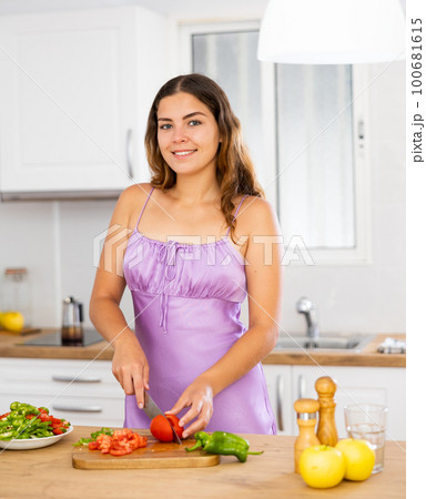 Young woman cooking vegetable salad in kitchen 100681615