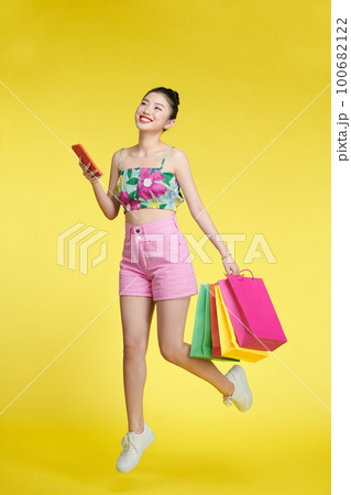 Full length of happy young attractive shopaholic woman raising shopping bags and holding mobile phone 100682122