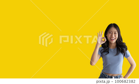 Young asian woman over yellow background doing ok sign with hands, OK symbol, Welcome, Agree, Join, Do as instructed, Follow orders, Acceptance of all conditions. Young asian woman over yellow background doing ok sign with hands, OK symbol, Welcome, Agree, Join, Do as instructed, Follow orders, Acceptance of all conditions. 100682382
