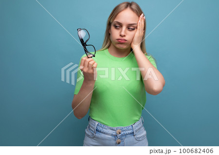 upset woman holding eyeglasses and holding her head on blue background upset woman holding eyeglasses and holding her head on blue background 100682406