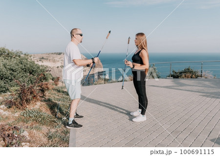 Happy Middle aged couple or friends practicing nordic walking in park near sea. Mature couple with trekking poles walking, practicing Nordic walking outdoors. Aging youthfully and sport concept Happy Middle aged couple or friends practicing nordic walking in park near sea. Mature couple with trekking poles walking, practicing Nordic walking outdoors. Aging youthfully and sport concept 100691115