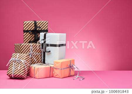Different sizes, colorful, striped and plain paper gift boxes tied with ribbons and bows on a pink surface and background. Close-up, copy space. Different sizes, colorful, striped and plain paper gift boxes tied with ribbons and bows on a pink surface and background. Close-up, copy space. 100691843