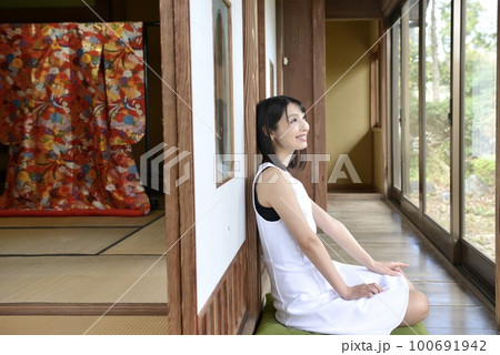 古民家の縁側でくつろぐ白いワンピースを着た微笑む若い女性 100691942