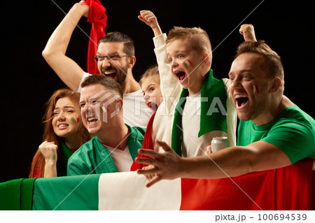 Excited people standing with flag of country. Football, soccer fans emotionally cheering up favourite team during match. Men visiting game with kids Excited people standing with flag of country. Football, soccer fans emotionally cheering up favourite team during match. Men visiting game with kids 100694539