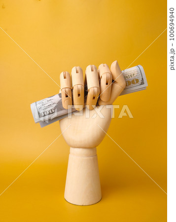Vertical view wooden hand gripping banknotes on a yellow background. 100694940
