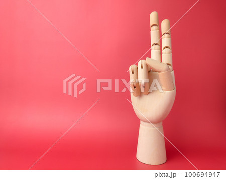 Wooden hand is pointing to a signal of peace on a red background with copy space. 100694947