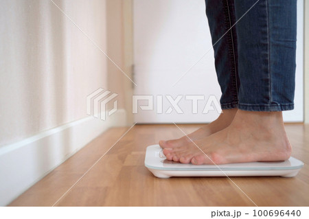 Unrecognizable woman stepping on the digital display weighting scale to measure her body weight and overall body mass index. Health care and wellbeing concept in modern people. 100696440