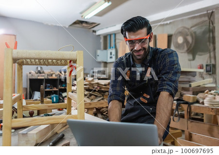 young carpenter caucasian man with laptop make drawing on wood to design at workspace. 100697695