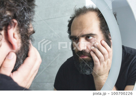 Middle-aged man looking tired and depressed in the bathroom mirror 100700226