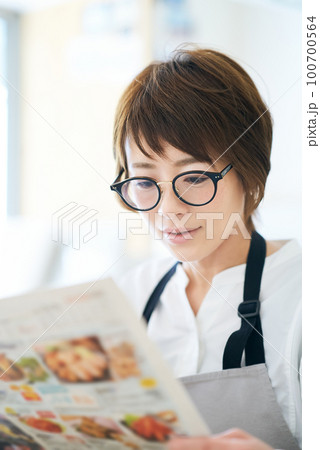 メガネをかけて広告チラシを見る女性 100700564