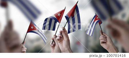 A group of people holding small flags of the Cuba in their hands A group of people holding small flags of the Cuba in their hands 100701416