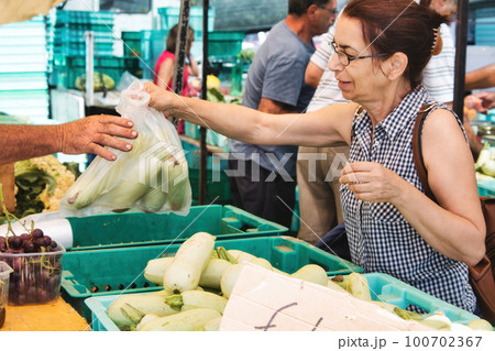 A middle-aged white Caucasian woman at an open-air food market buying a bag of vegetables 100702367