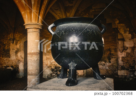 A big black cast iron metal cauldron in a medieval castle basement under an arch 100702368