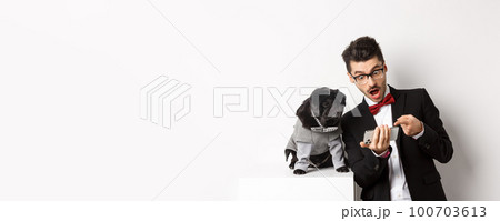 Amazed man showing video to dog, pointing at mobile phone and look excited while pug sitting unbothered in costume, white background Amazed man showing video to dog, pointing at mobile phone and look excited while pug sitting unbothered in costume, white background 100703613