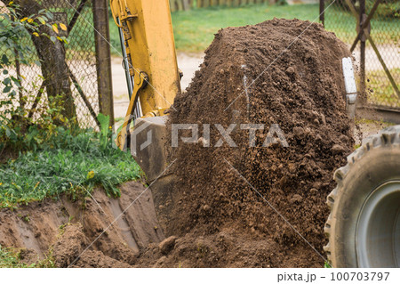 A bucket of a bulldozer digs the ground with a grass close-up in an industrial area. Excavation work on the construction site A bucket of a bulldozer digs the ground with a grass close-up in an industrial area. Excavation work on the construction site 100703797
