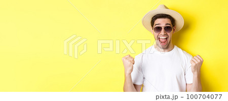 Concept of tourism and holidays. Lucky man tourist winning tickets, making fist pump and saying yes, wearing vacation clothes, standing over yellow background 100704077