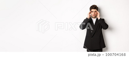 Image of businessman in black suit, touching head and looking dizzy, feeling painful headache, standing over white background Image of businessman in black suit, touching head and looking dizzy, feeling painful headache, standing over white background 100704168