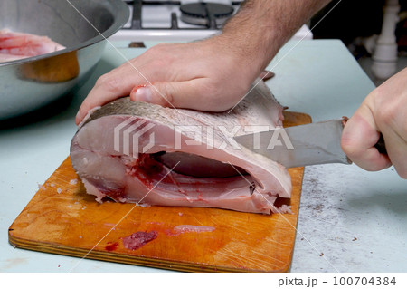 Man prepares fresh silver carp fish. Cuts it into steaks with a knife. home cooking concept 100704384