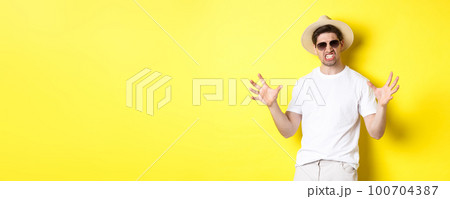 Tourism, travelling and holidays concept. Sassy young man on vacation, showing something big and clenching teeth, standing in sunglasses and summer hat 100704387