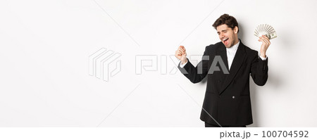 Portrait of handsome and successful businessman in suit, dancing with money, standing against white background Portrait of handsome and successful businessman in suit, dancing with money, standing against white background 100704592