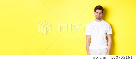 Disappointed guy looking upset, sulking and frowning, standing displeased against yellow background 100705161