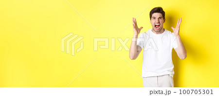 Angry man yelling and shaking hands, grimacing with hatred, standing hateful against yellow background 100705301