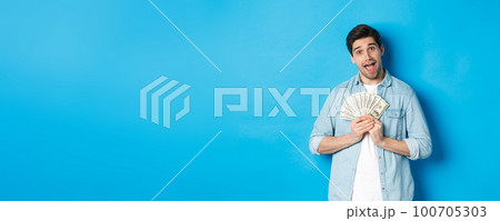 Smiling greedy guy hugging money and smiling, unwilling to share, standing over blue background 100705303