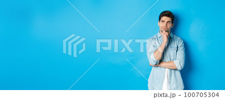 Image of adult bearded man 25s years, thinking about something, looking at upper left corner and pondering ideas, standing over blue background 100705304
