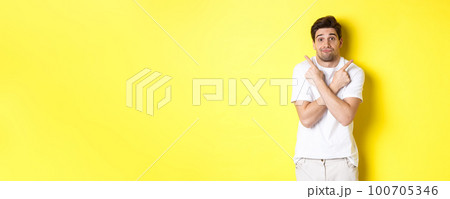 Indecisive man pointing fingers sideways, struggling to make decision, asking advice, standing over yellow background Indecisive man pointing fingers sideways, struggling to make decision, asking advice, standing over yellow background 100705346