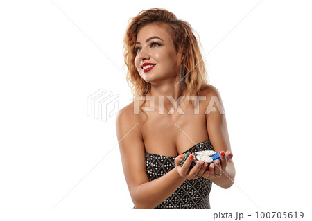 Ginger girl in gray dress posing holding a lot of colorful chips in her palms standing isolated on white background. Casino, poker. Close-up shot. 100705619