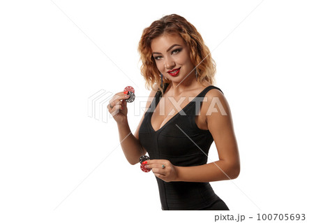 Ginger girl wearing a black dress is posing holding red and green chips in her hands standing isolated on white background. Casino, poker. Close-up. Ginger girl wearing a black dress is posing holding red and green chips in her hands standing isolated on white background. Casino, poker. Close-up. 100705693