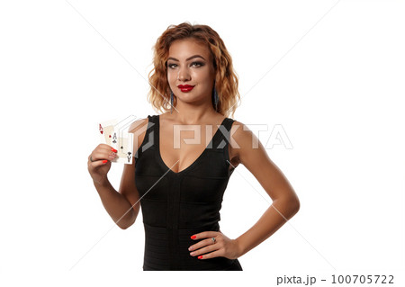 Ginger girl wearing a black dress is posing holding two playing cards in her hands standing isolated on white background. Casino, poker. Close-up. Ginger girl wearing a black dress is posing holding two playing cards in her hands standing isolated on white background. Casino, poker. Close-up. 100705722