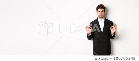 Concept of new year party, celebration and lifestyle. Portrait of confident good-looking man in black suit, showing okay sign and approve something, standing over white background Concept of new year party, celebration and lifestyle. Portrait of confident good-looking man in black suit, showing okay sign and approve something, standing over white background 100705849