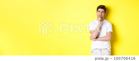Portrait of young male model thinking, looking at upper left corner and making choice, standing near copy space, yellow background Portrait of young male model thinking, looking at upper left corner and making choice, standing near copy space, yellow background 100706416