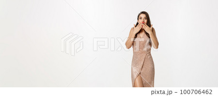 Party and celebration concept. Full-length of beautiful woman in elegant dress, standing near Christmas gifts and looking surprised, standing over white background 100706462