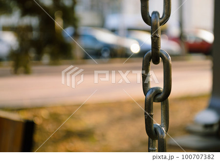 The links of a metal chain hang vertically and are illuminated by the evening sun The links of a metal chain hang vertically and are illuminated by the evening sun 100707382