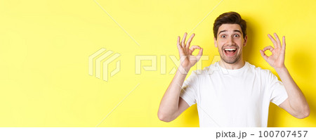 Amazed young man showing ok signs and smiling, recommending something good, standing over yellow background satisfied 100707457