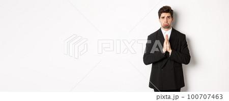 Miserable clingy guy need help, pouting silly and begging for something, asking for favour, standing against white background in black suit Miserable clingy guy need help, pouting silly and begging for something, asking for favour, standing against white background in black suit 100707463