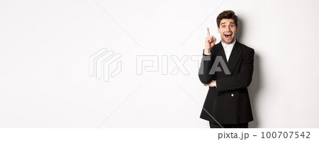 Portrait of attractive man in suit, having an idea, standing excited and raising one finger to tell suggestion, think-up solution, standing over white background Portrait of attractive man in suit, having an idea, standing excited and raising one finger to tell suggestion, think-up solution, standing over white background 100707542