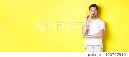 Thoughtful guy suggesting solution, raising finger in eureka sign and looking excited, have an idea, standing against yellow background 100707919