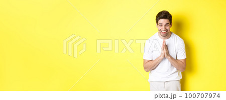 Handsome guy saying thank you, bowing and holding hands in namaste gesture, express gratitude, standing over yellow background 100707974