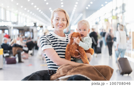 Mother traveling with child, holding his infant baby boy at airport terminal waiting to board a plane. Travel with kids concept Mother traveling with child, holding his infant baby boy at airport terminal waiting to board a plane. Travel with kids concept 100708046