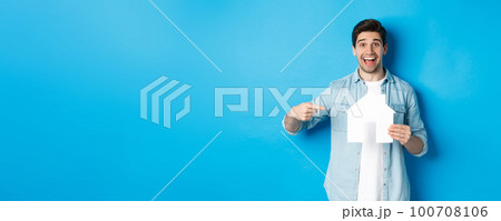 Insurance, mortgage and real estate concept. Surprised man pointing at house model and smiling, searching apartment to rent or buy, standing against blue background Insurance, mortgage and real estate concept. Surprised man pointing at house model and smiling, searching apartment to rent or buy, standing against blue background 100708106