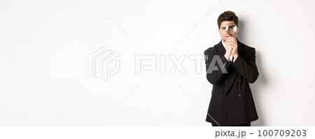 Image of serious businessman in black trendy suit, looking through magnifying glass, looking for employees, standing against white background Image of serious businessman in black trendy suit, looking through magnifying glass, looking for employees, standing against white background 100709203