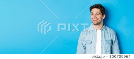 Young modern guy with beard, looking left and smiling pleased at copy space, standing over blue background Young modern guy with beard, looking left and smiling pleased at copy space, standing over blue background 100709964