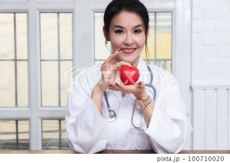 Female doctor holding a red heart ball in the hospital. Concept of health care and medical. Female doctor holding a red heart ball in the hospital. Concept of health care and medical. 100710020