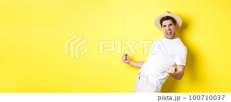 Concept of tourism and vacation. Satisfied young male tourist celebrating, winning something and rejoicing, making fist pump and shouting yes, standing against yellow background 100710037