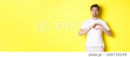 Cute guy pucker lips and waiting for kiss, showing heart gesture. Concept of love and romance 100710249