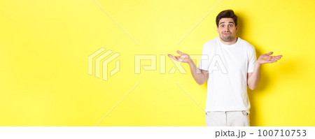 Clueless man shrugging, spread hands sideways confused, dont know anything, standing over yellow background Clueless man shrugging, spread hands sideways confused, dont know anything, standing over yellow background 100710753