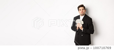 Image of greedy guy in black suit, holding money and unwilling to share, standing over white background Image of greedy guy in black suit, holding money and unwilling to share, standing over white background 100710769